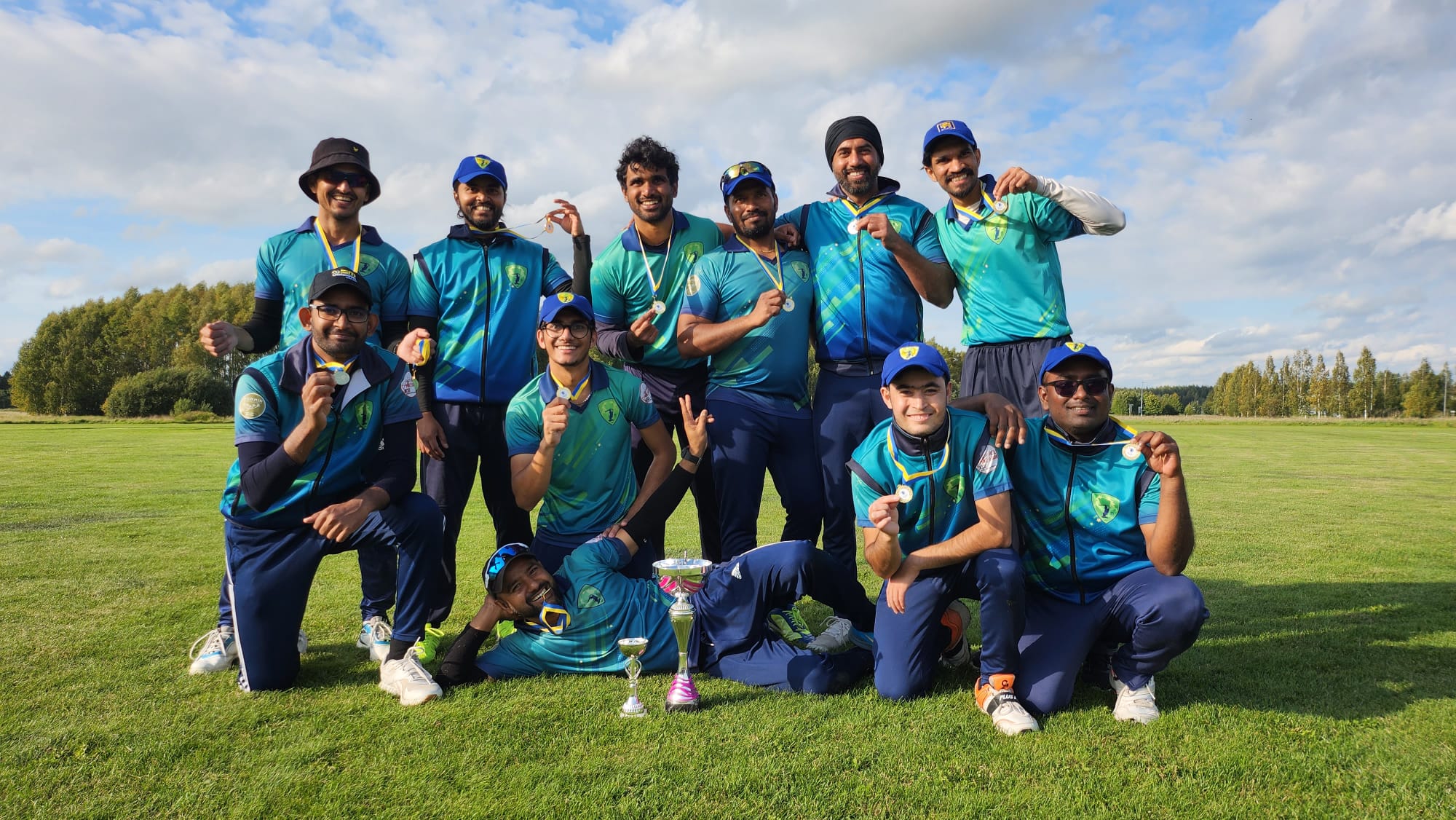 Ett cricketlag från Umeå vann en turnering, de står uppställda med sin pokal på planen och ler mot kameran. De är 11 spelare.